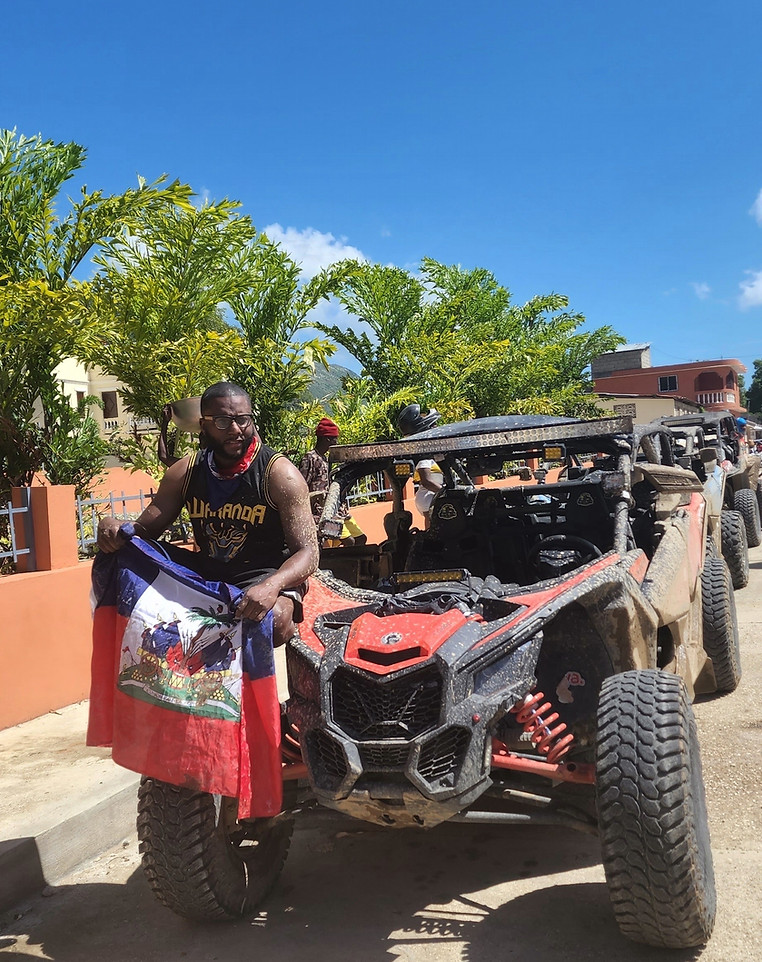 Avivaa rider holding the Haitian flag beside a Can-Am Maverick UTV in Cap-Haïtien